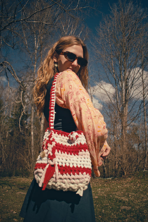 Woman holding a red and white crocheted bag outdoors