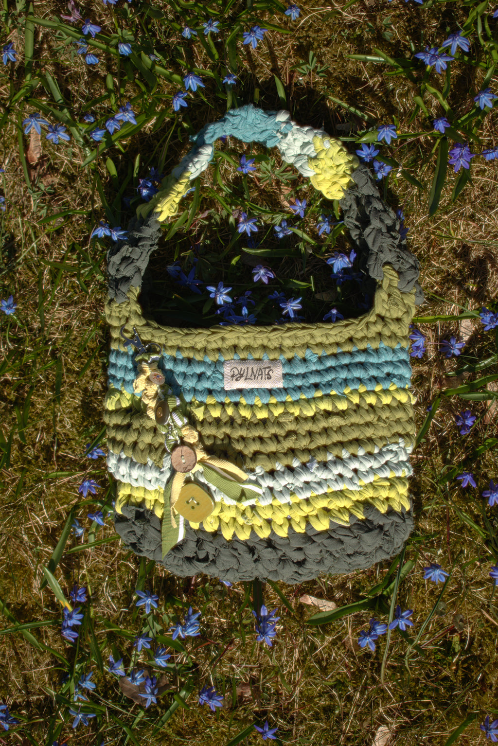 Knitted bag with colorful patterns on a grassy background with small blue flowers.