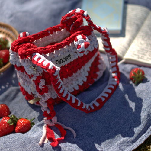 Red and white knitted bag on a blue blanket with strawberries around