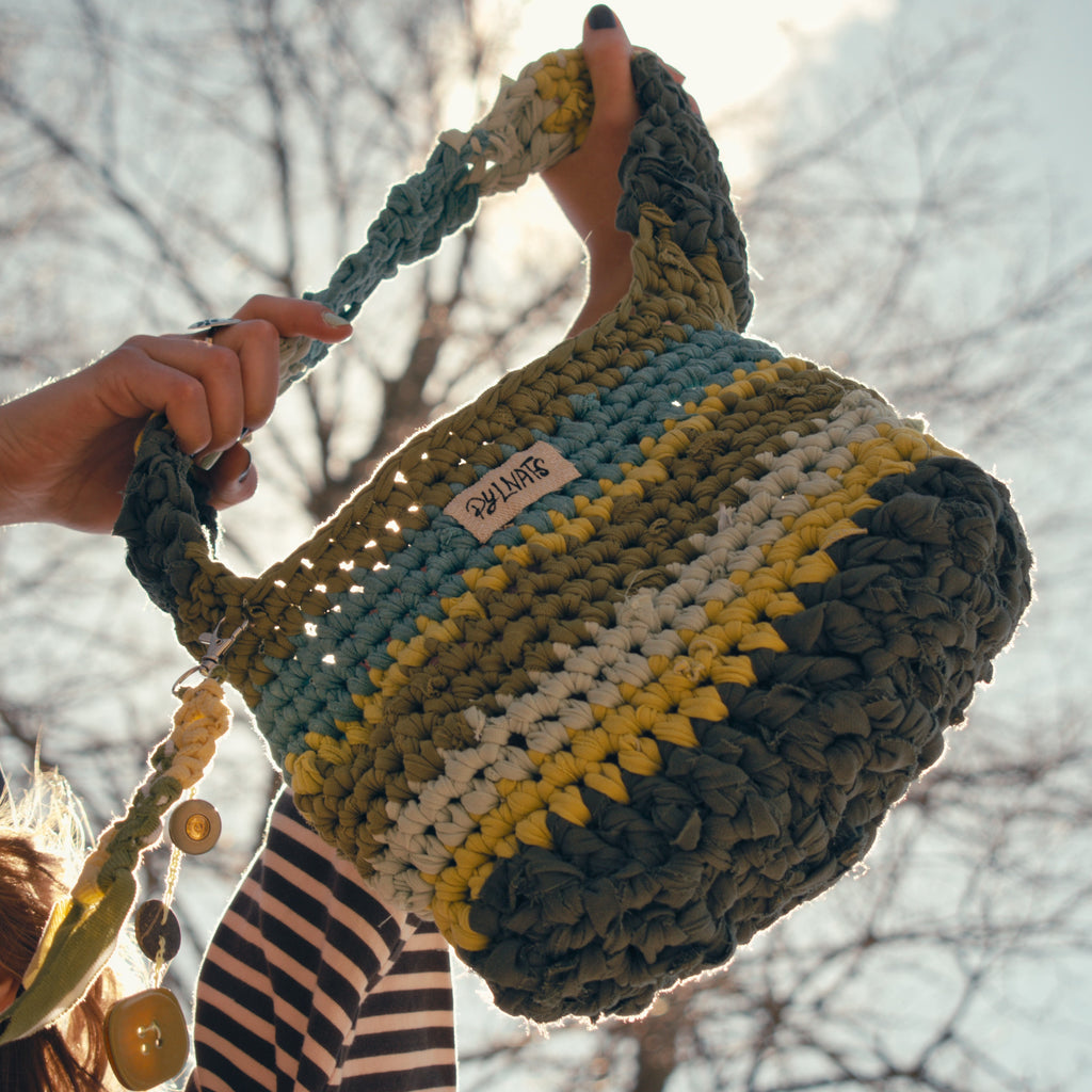Handmade crochet bag with a visible brand label held by a person outdoors.